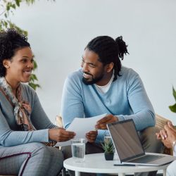 Young African American couple and their insurance agent talking while going through paperwork during the meeting.